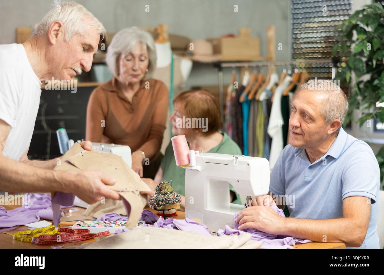 Some people communicate and discuss pattern, while others sew using sewing machine at lesson Stock Photo