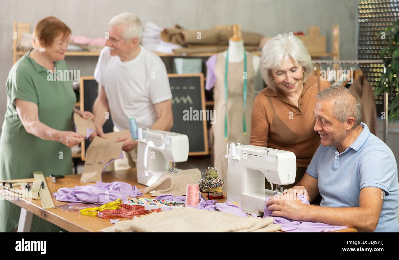 Some people communicate and discuss pattern, while others sew using sewing machine at lesson Stock Photo