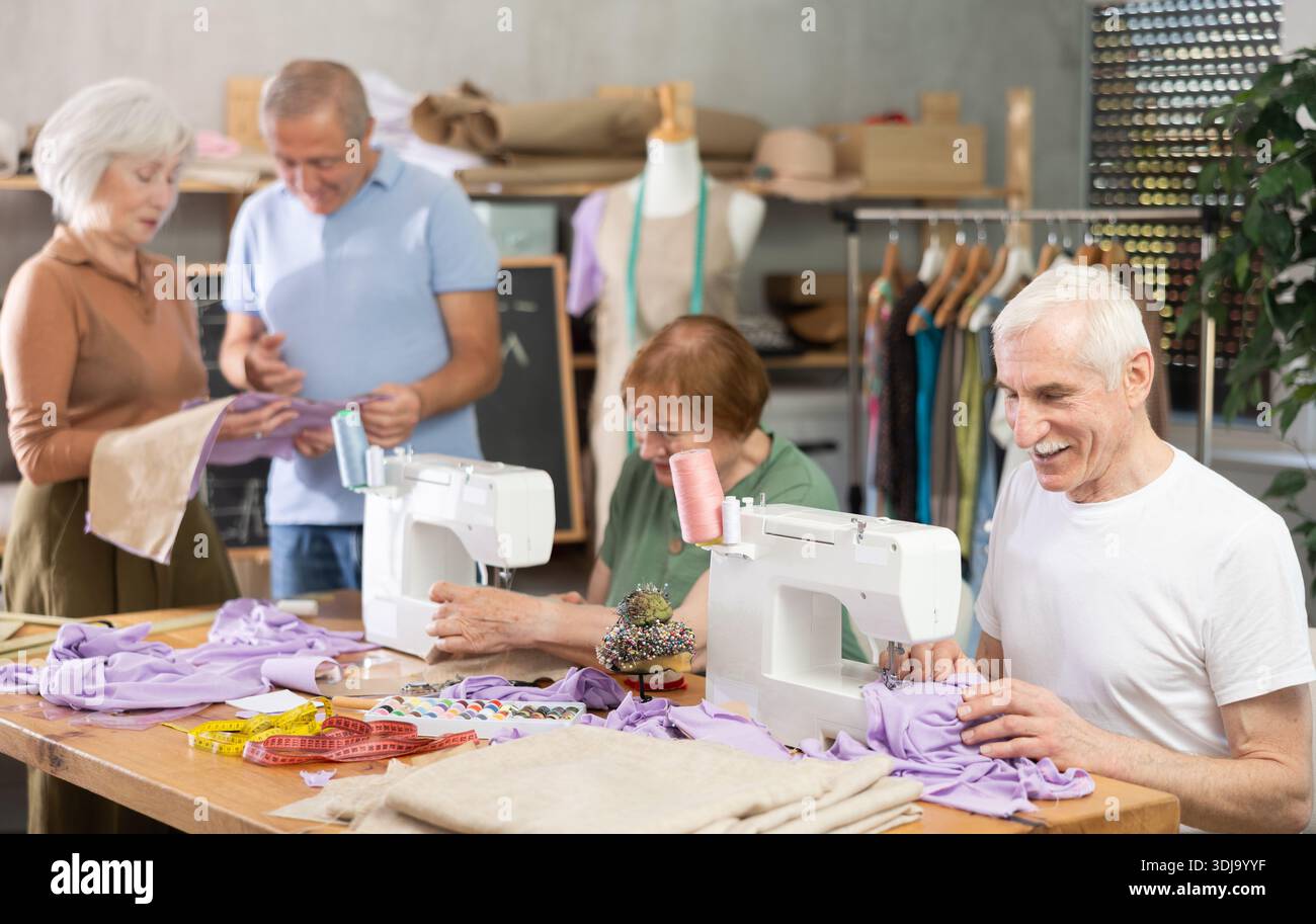 Some people communicate and discuss pattern, while others sew using sewing machine at lesson Stock Photo