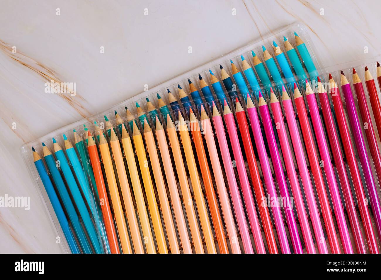 Collection of drawing pencils shows different colors in clear case on plain surface. Stock Photo