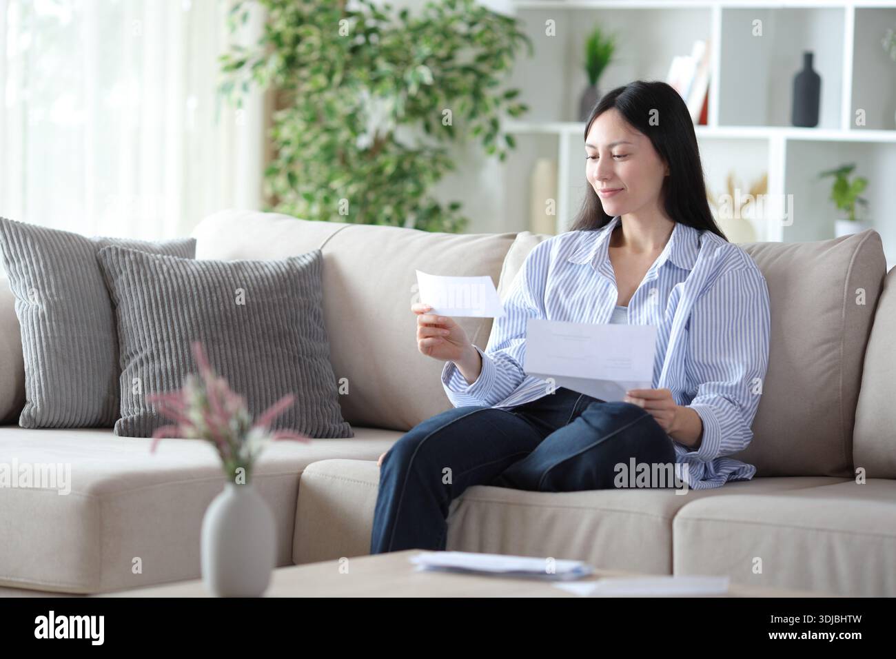 Asian woman checking letter sitting on a sofa at home Stock Photo