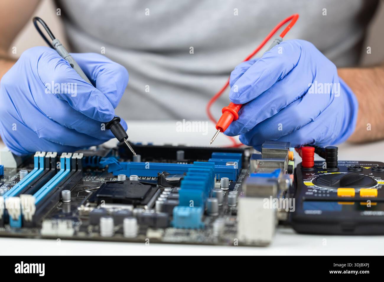 Testing motherboard with probes and multimeter, Close-up of technician using probes on computer motherboard with red multimeter during electronic diag Stock Photo