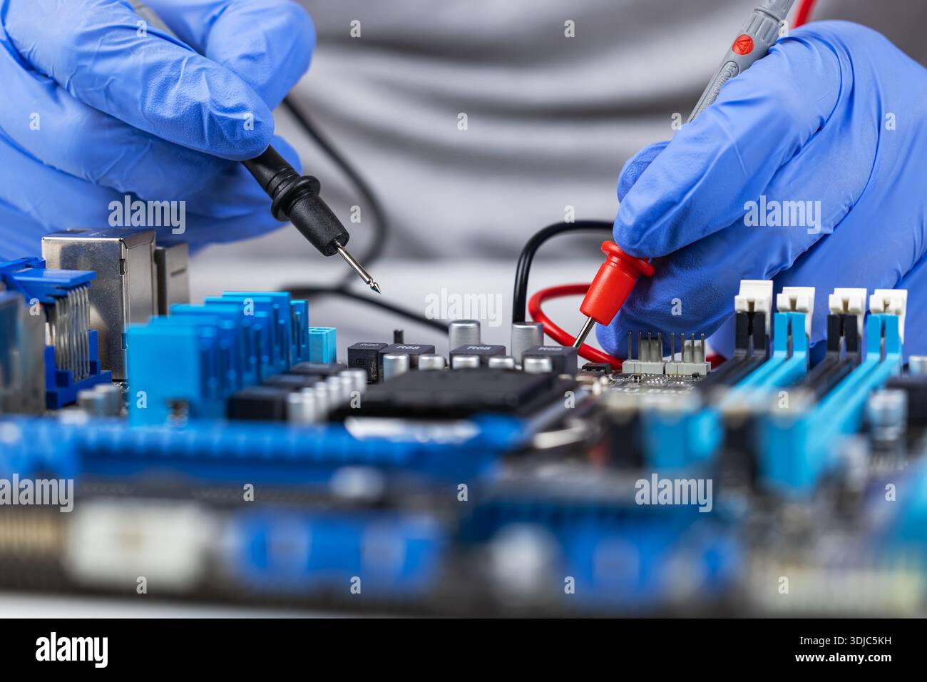 Testing motherboard with probes and multimeter, Close-up of technician using probes on computer motherboard with red multimeter during electronic diag Stock Photo