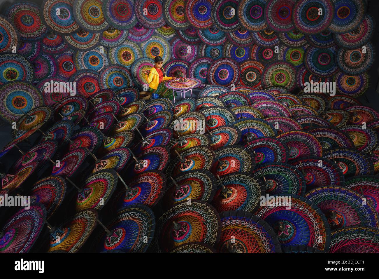 Young Burmese woman sitting on a stool in a workshop making traditional colourful Pathein Umbrellas (Pathein hti), Myanmar Stock Photo