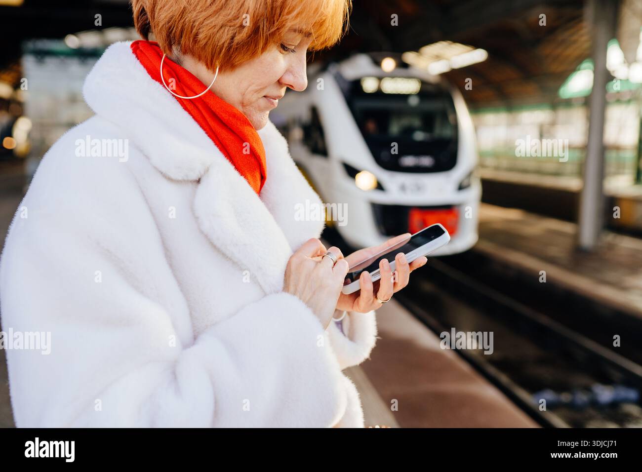 Caucasian redhead woman using smartphone on railway platform Stock Photo