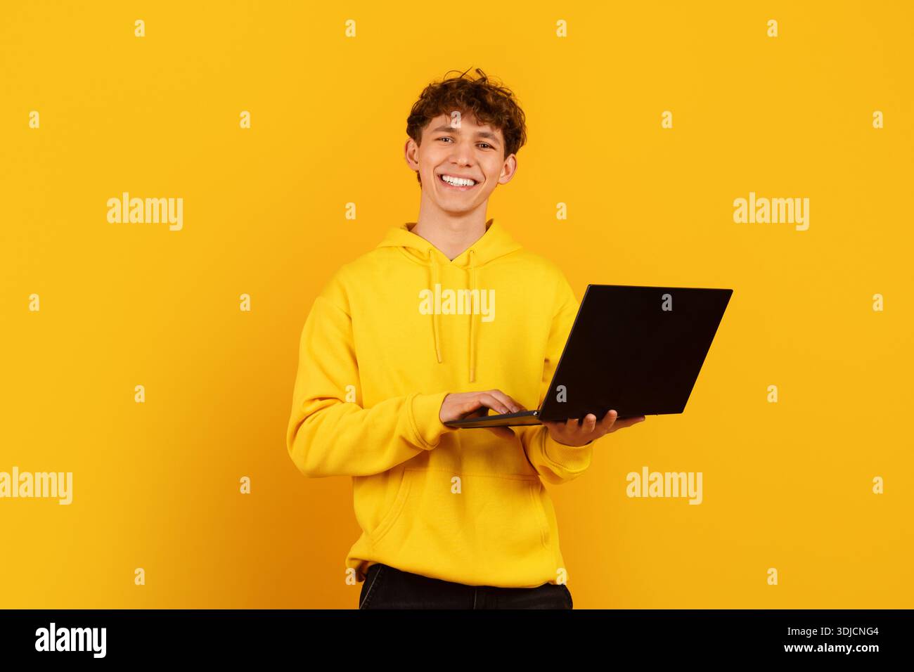 Cheerful young man using laptop on bright yellow background, representing remote work Stock Photo