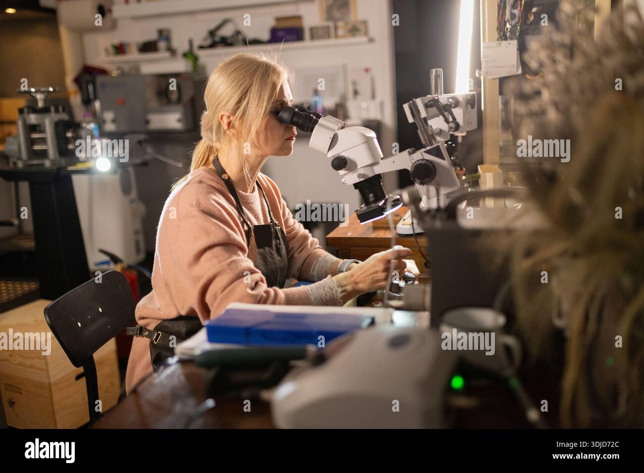 Woman examining jewelry details using microscope in workshop Stock Photo