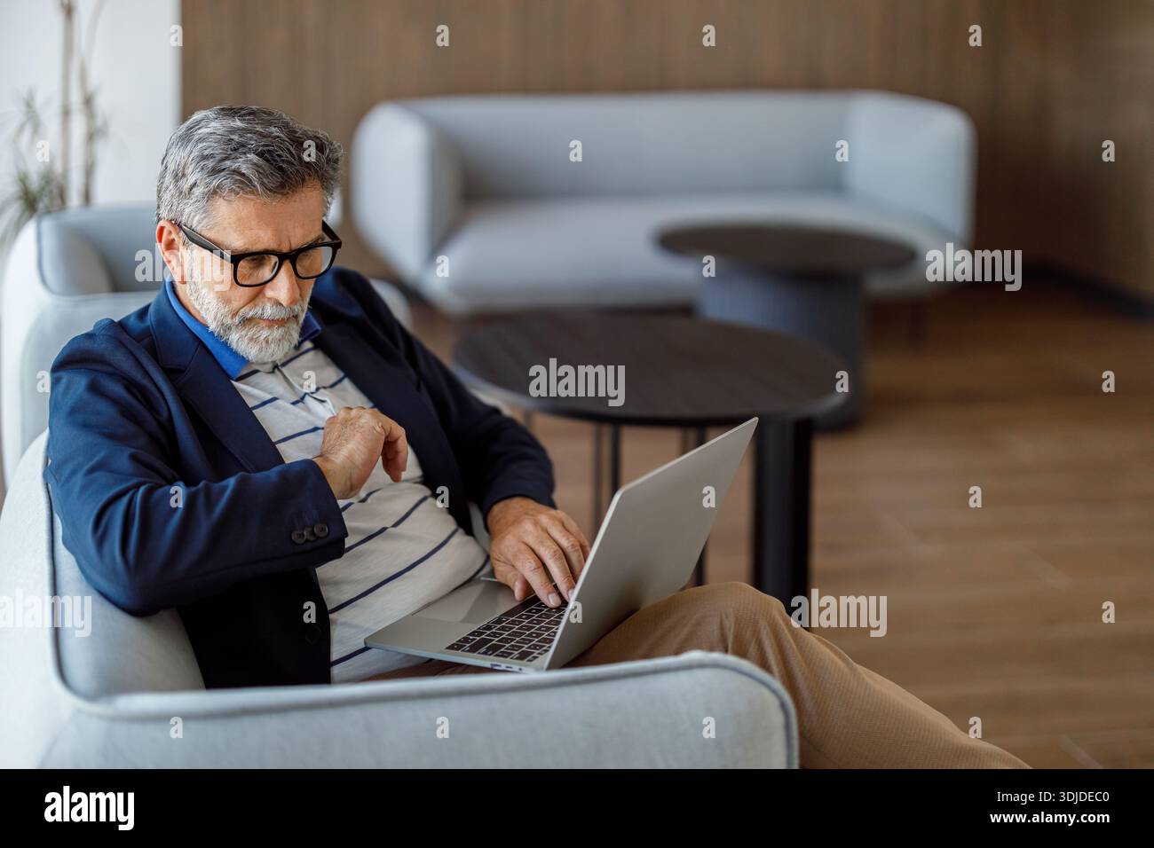 Focused bearded male professional doing online research over laptop while sitting on sofa in corporate office Stock Photo
