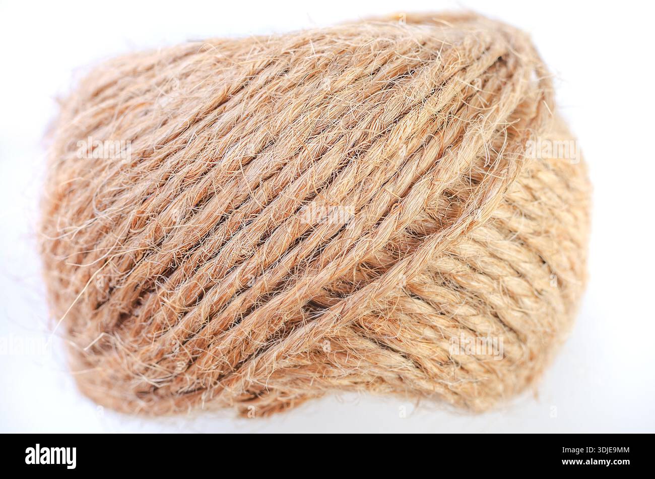 Close-up macro shot of a tightly wound ball of natural jute twine on a white background Stock Photo
