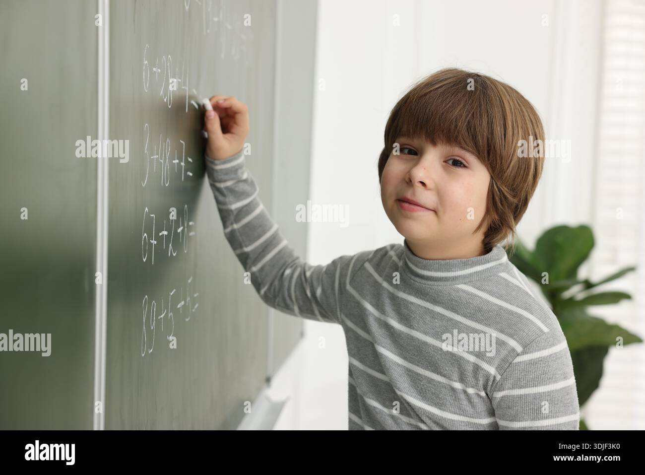 Schoolboy doing math on chalkboard in classroom Stock Photo