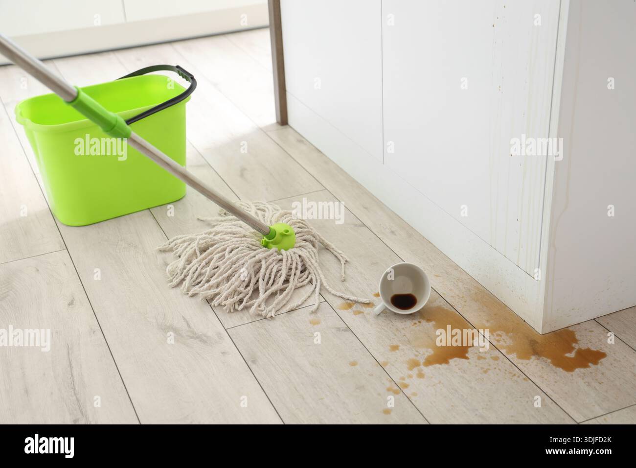 Overturned cup, spilled coffee and mop on floor in kitchen Stock Photo