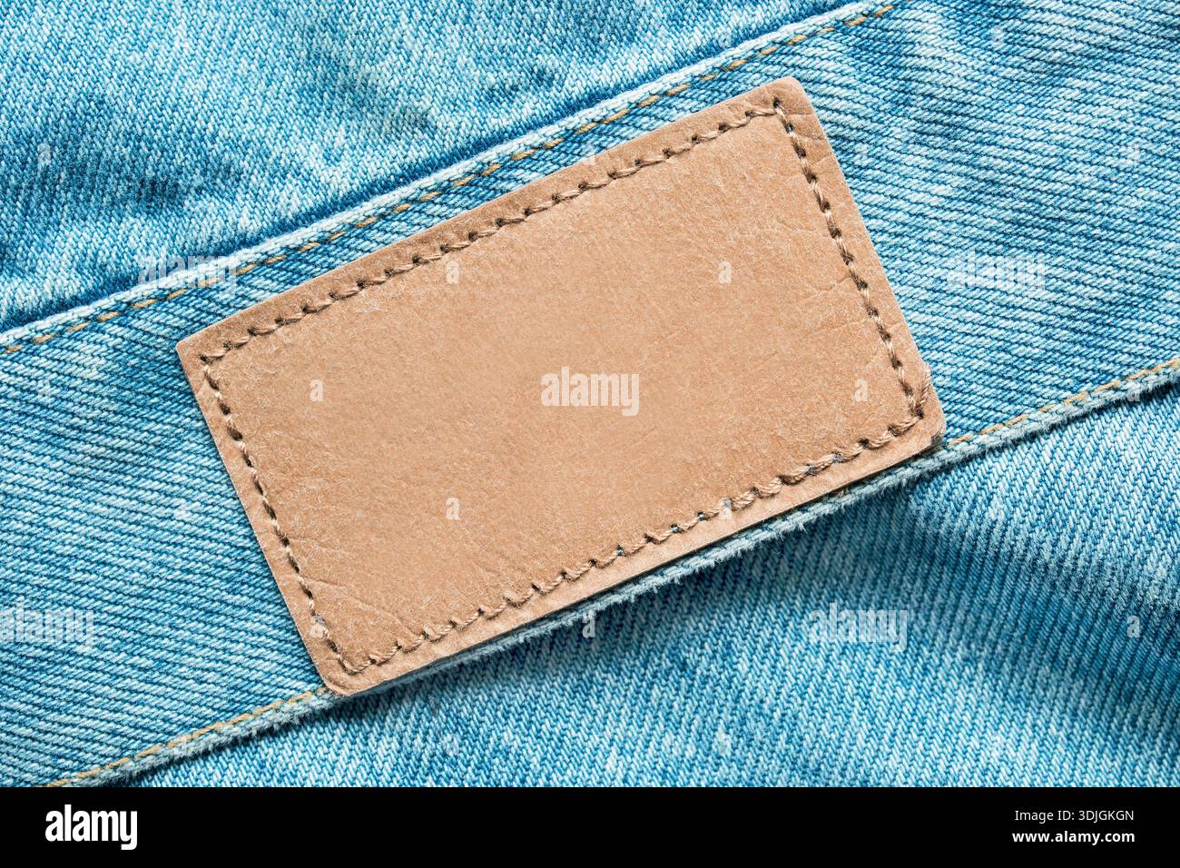 Empty patch label stitched on light blue denim fabric background closeup Stock Photo