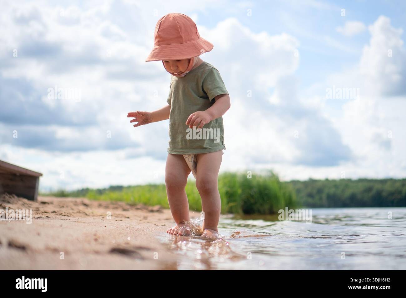 A child plays in the water with an orange hat, splashing and enjoying the coolness of the sea. Stock Photo