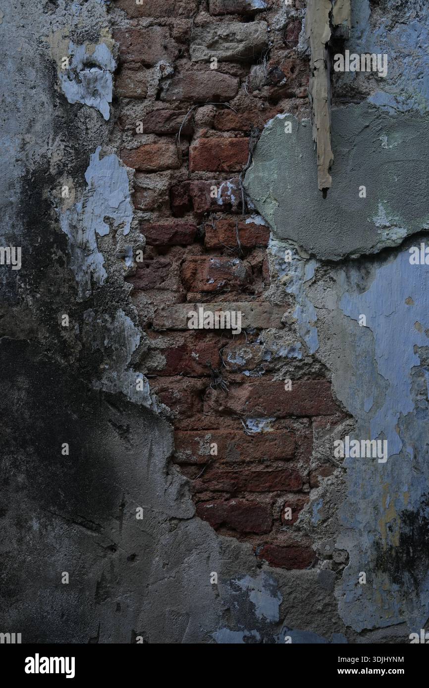 Exposed brickwork reveals layered plaster decay, highlighting aging construction materials and surface deterioration. Stock Photo