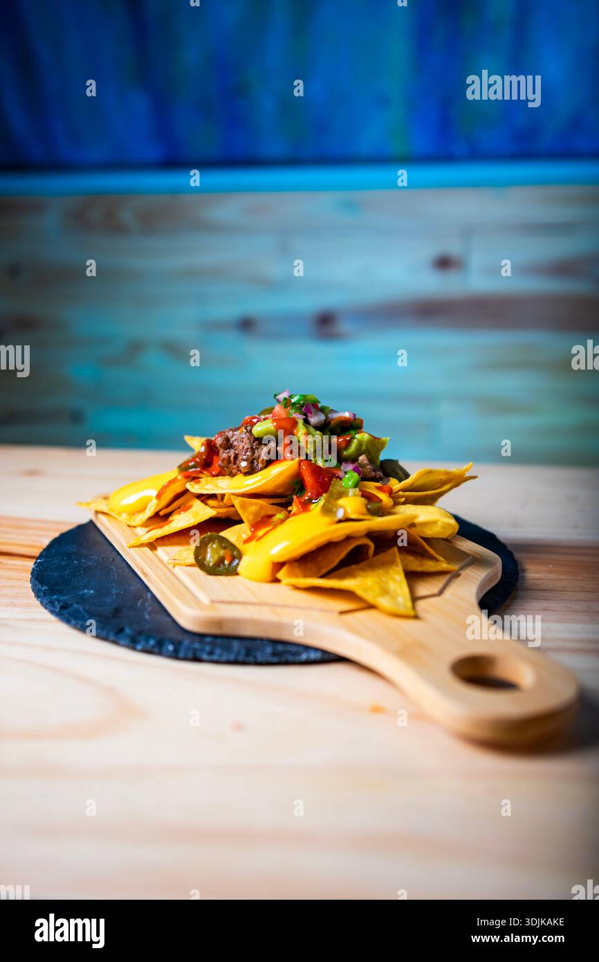 Nachos serving on a wooden board with melted cheese, beef, guacamole, and salsa Stock Photo