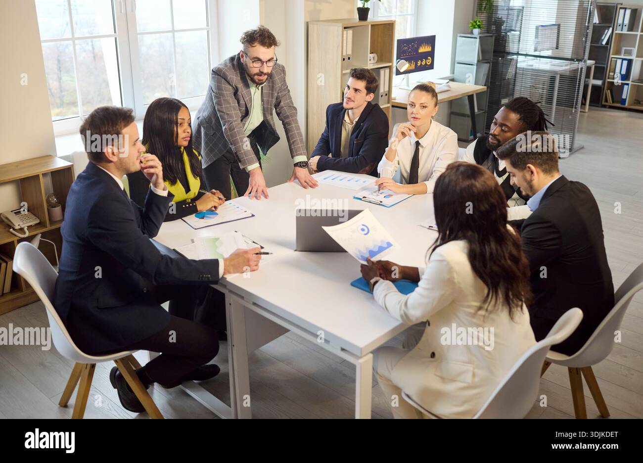 Manager leads office team briefing at table, analyzing charts and strategy Stock Photo