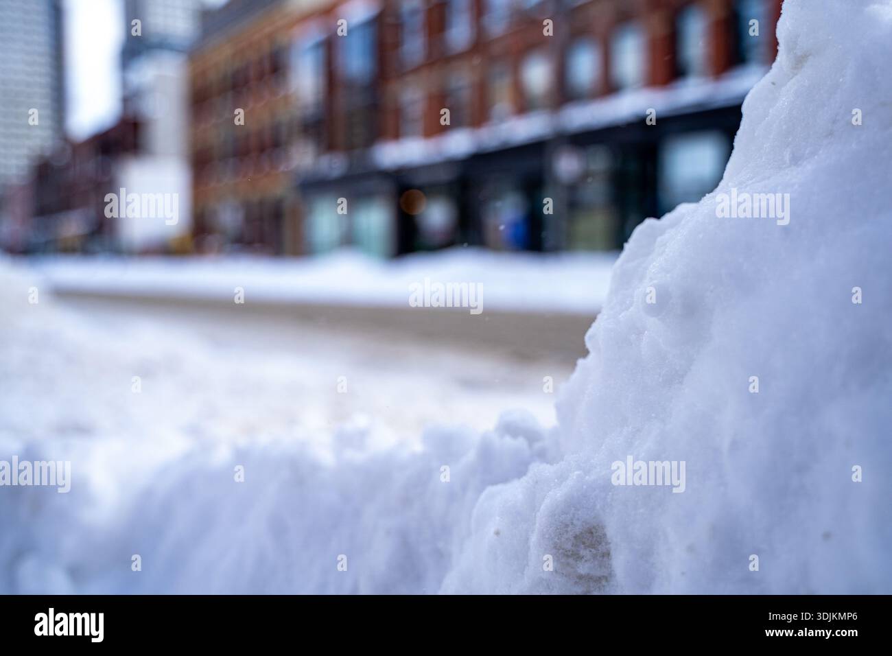 Close up of snow piled along the roadside with blurred street background. Stock Photo