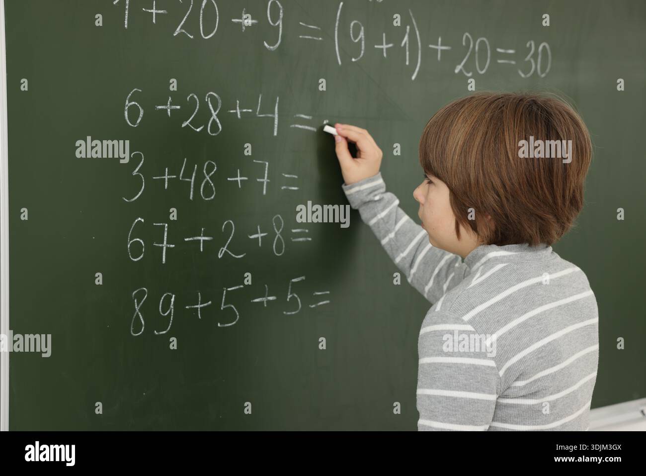 Schoolboy doing math on chalkboard in classroom Stock Photo