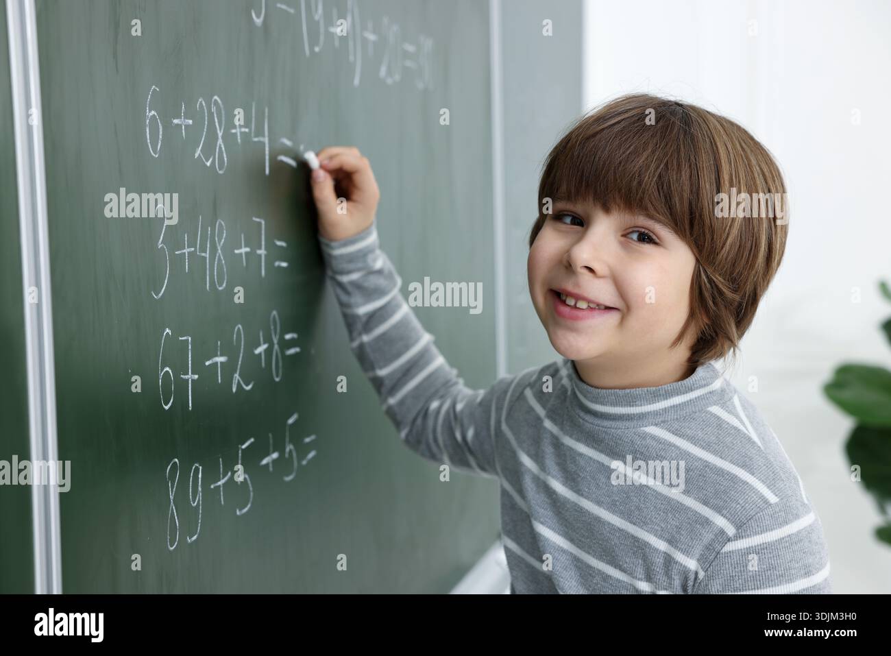Schoolboy doing math on chalkboard in classroom Stock Photo