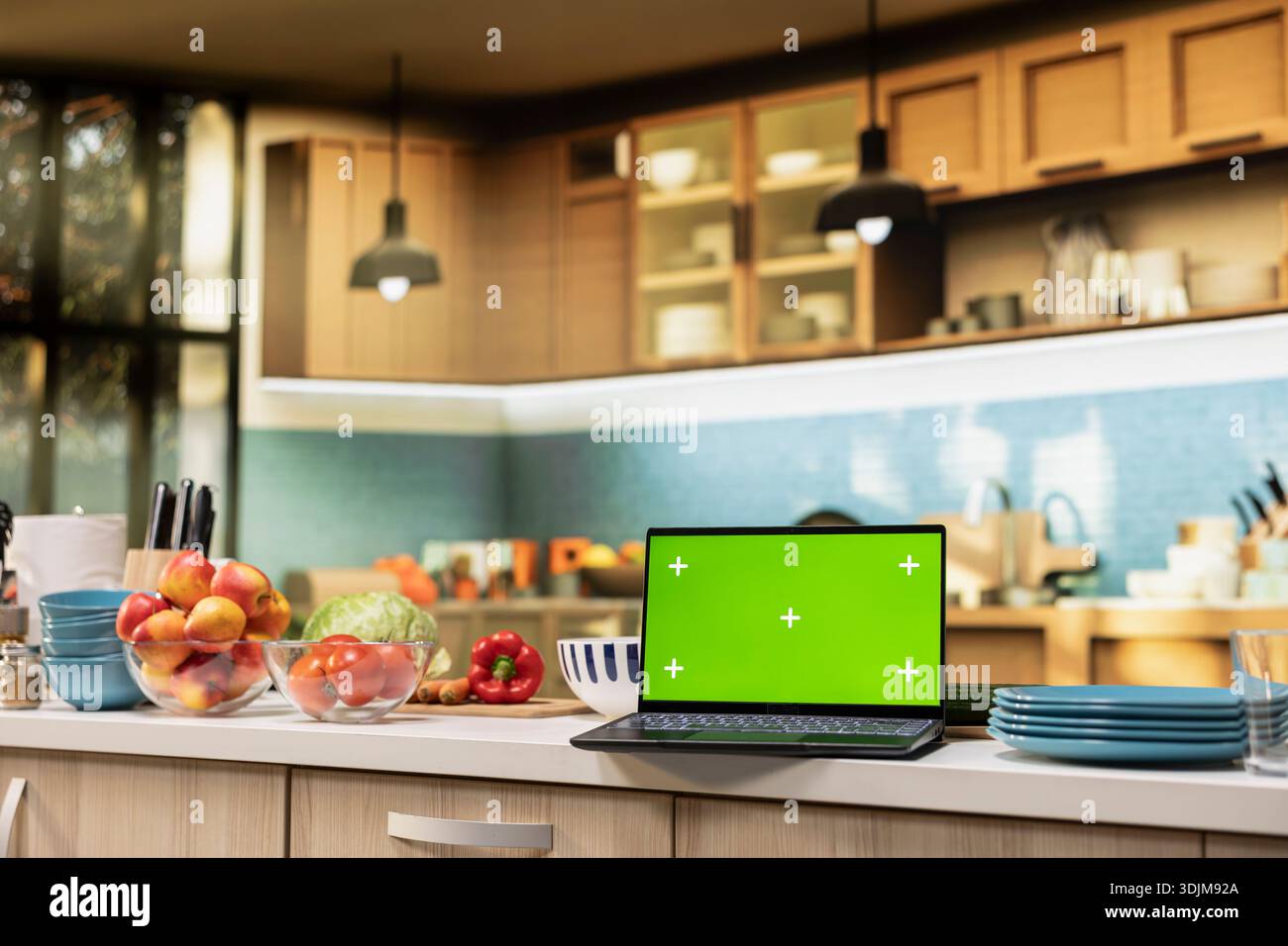 Green screen on laptop in the kitchen with rustic counter and elegant lighting. Cookware and utensils creating a comfortable and inviting household dining space with modern interior design. Stock Photo