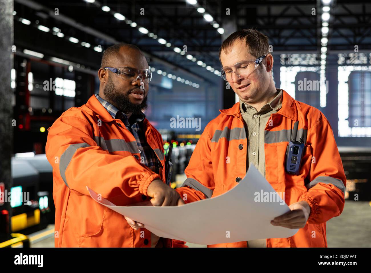 Diverse operators handling assembly workflow with industrial plans ...