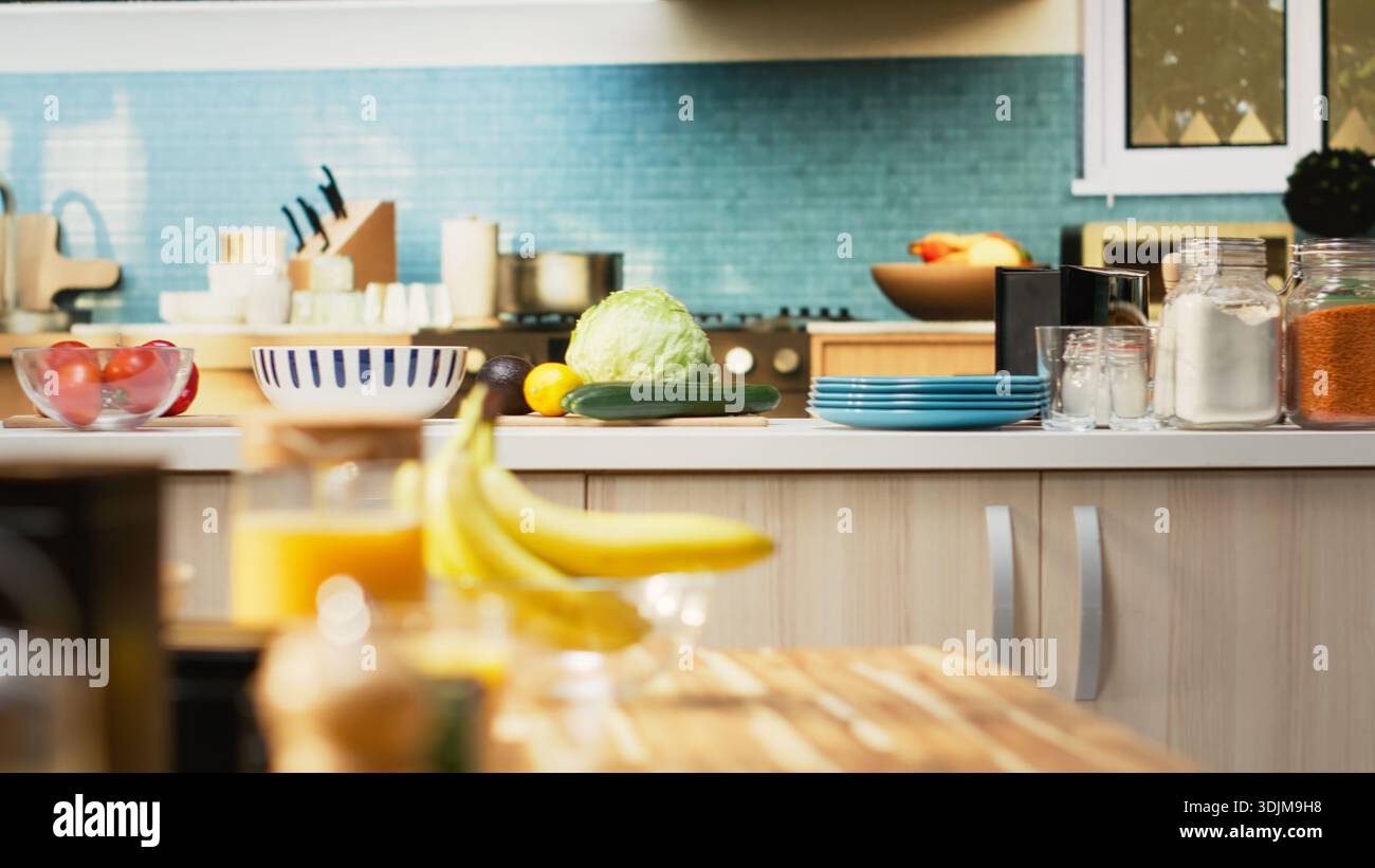 Bright modern kitchen interior with elegant furniture and wooden cupboards. Cookware and fresh vegetables on a cutting board, showcasing a stylish household and luxury home design. Stock Photo