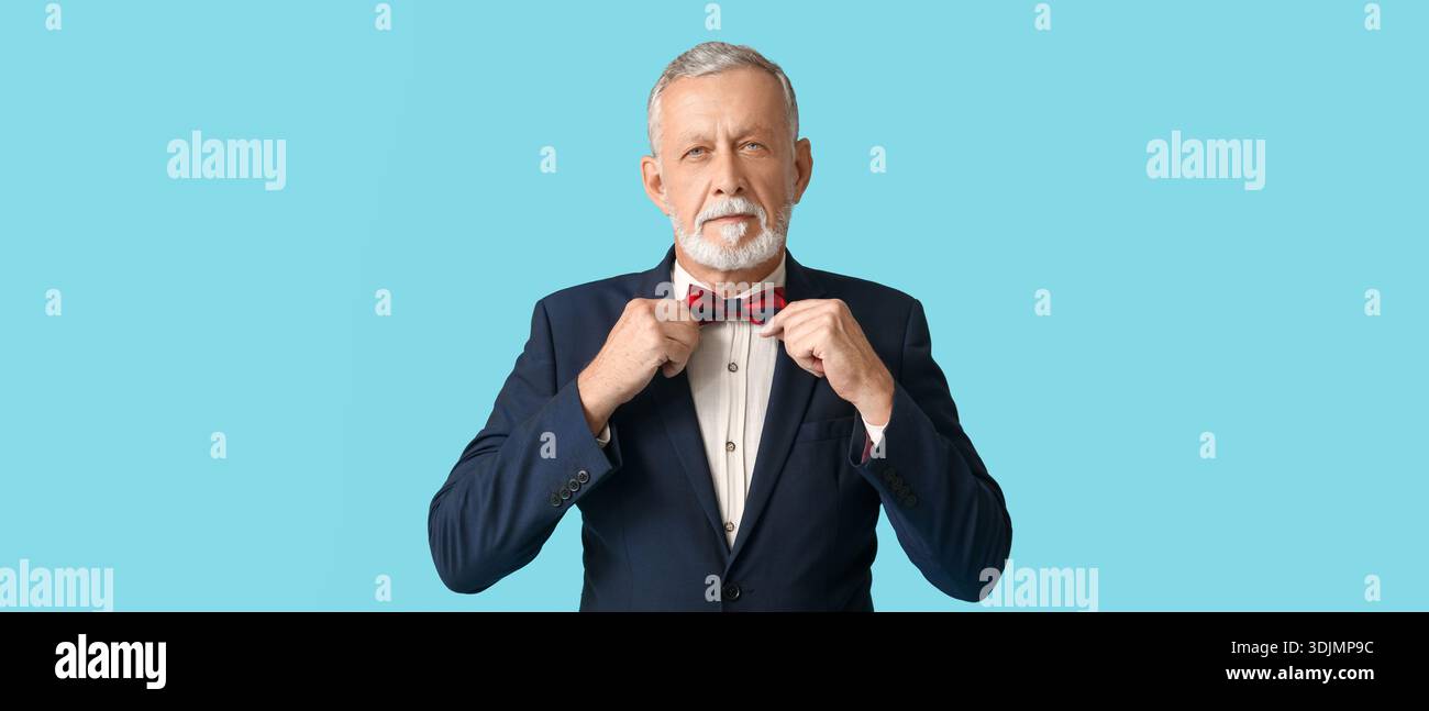 Handsome mature man in stylish formal suit adjusting bow tie on blue background Stock Photo