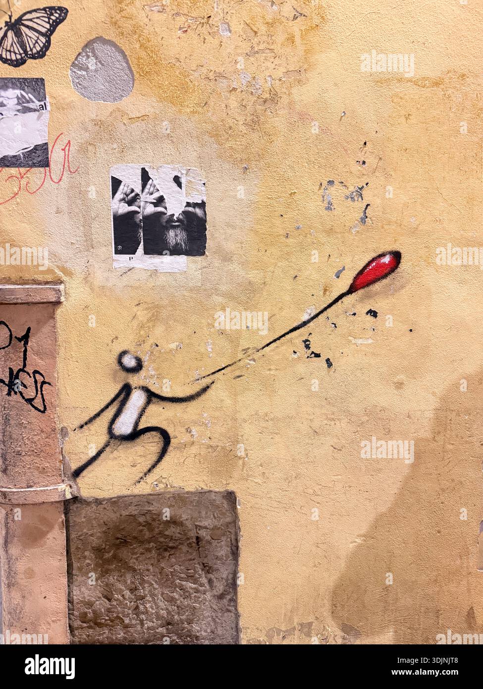 A textured, weathered yellow wall in Florence features urban art. Stock Photo
