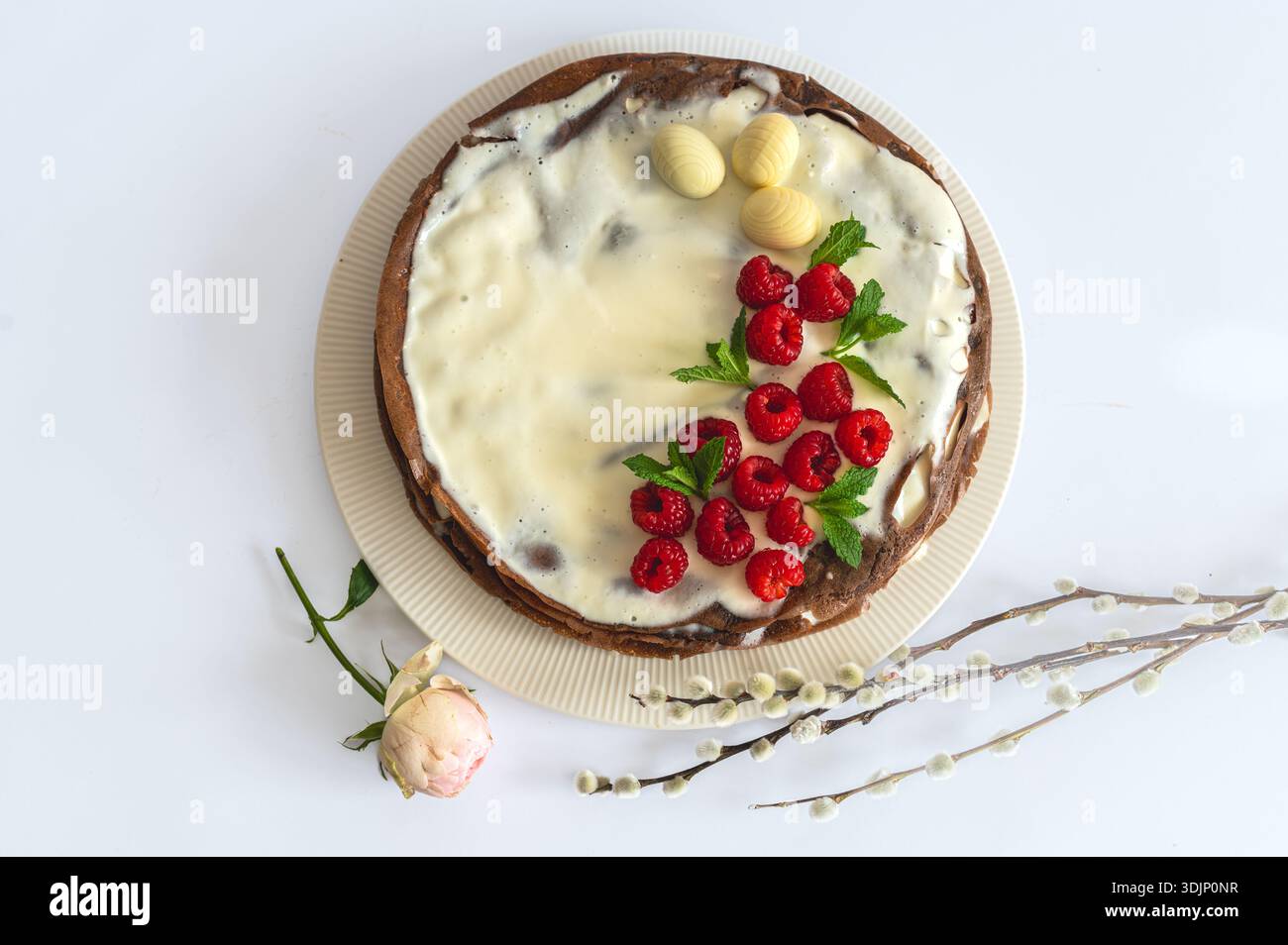 Festive Easter greeting with raspberry cake, floral elements, willow branch arranged on white. Stock Photo