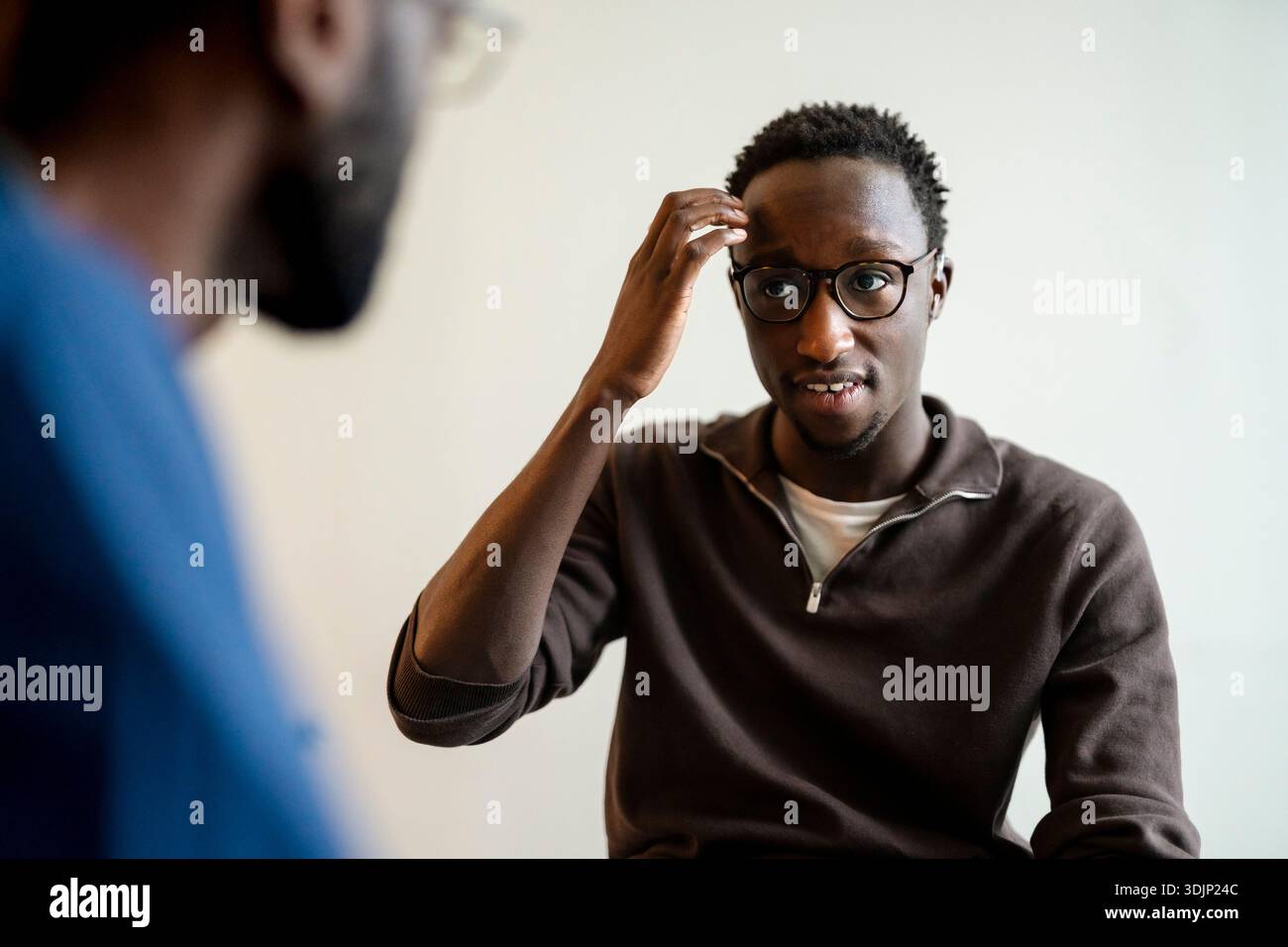 Young man with hearing problem using sign language while communicating with doctor in clinic Stock Photo