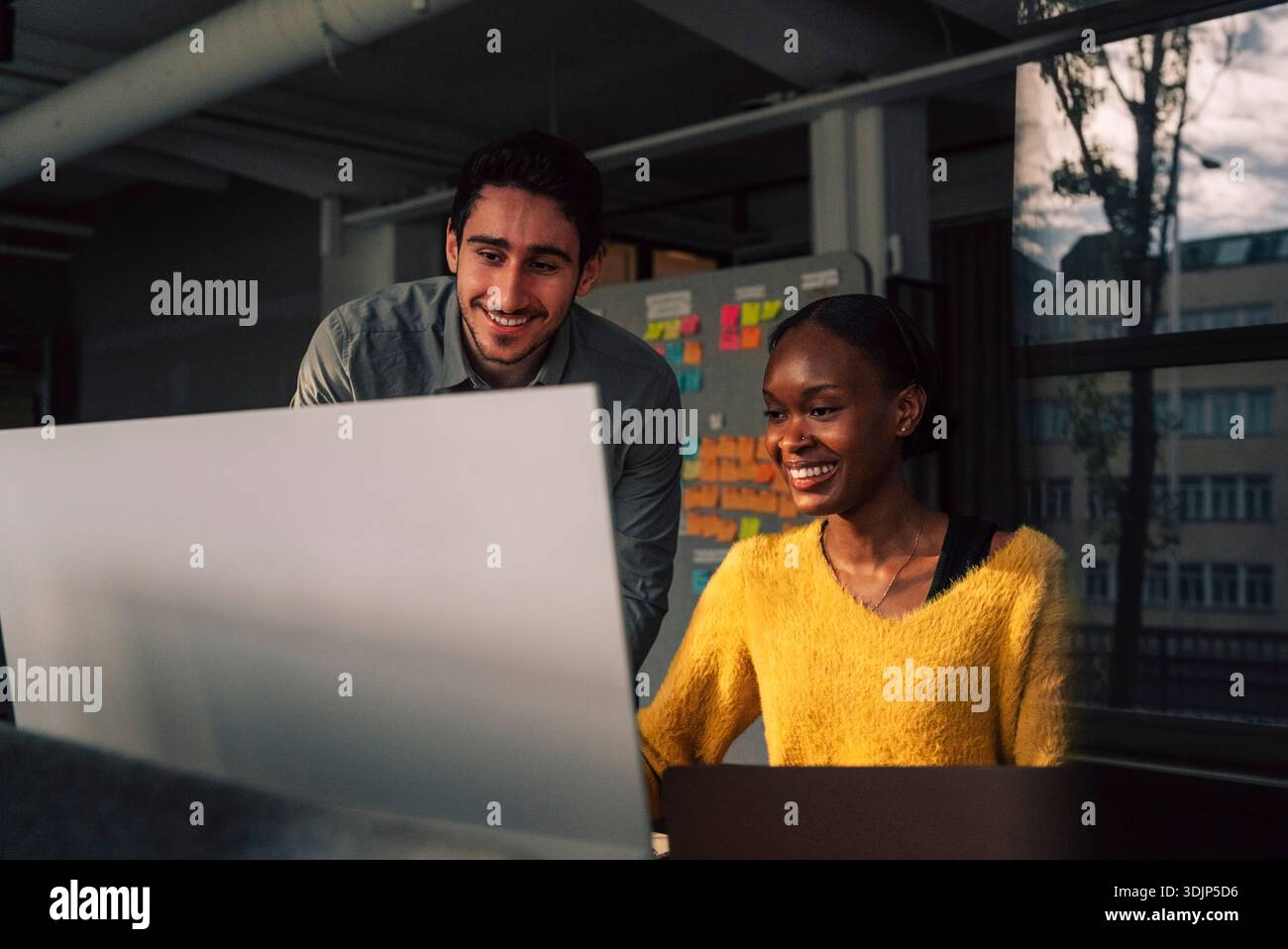 Smiling female programmer using computer while sitting beside male colleague in tech office Stock Photo