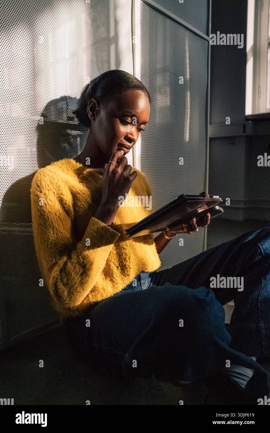 Concentrated female business expert using tablet PC while sitting on ground in startup office Stock Photo