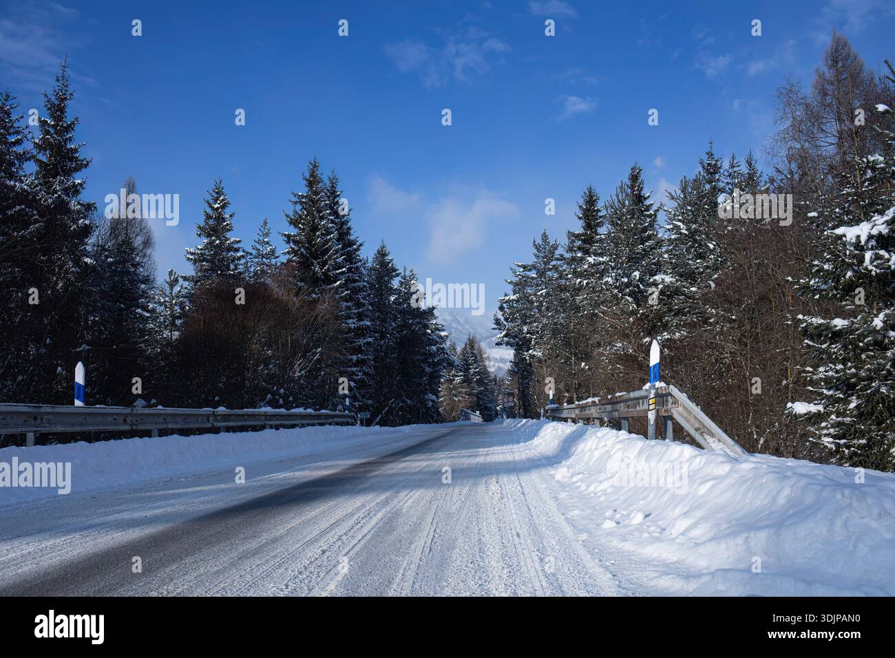 Snowy Winter Road Through Forest Under Blue Sky Stock Photo