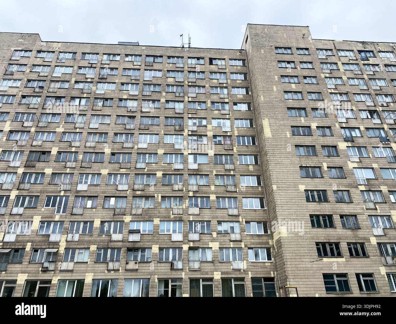 Unappealing dormitory structure featuring many windows and air conditioning units, set against a cloudy sky in an urban environment Stock Photo