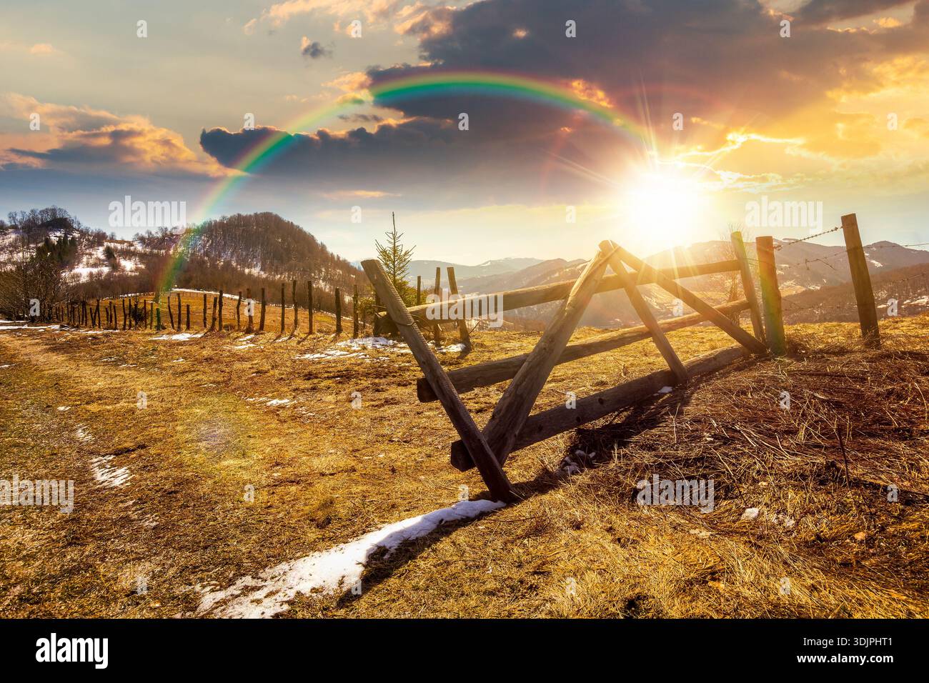 rural landscape of carpathian mountains in early spring under blue sky at sunset. snow covered hill with barbed wire fence on in evening light. storyt Stock Photo