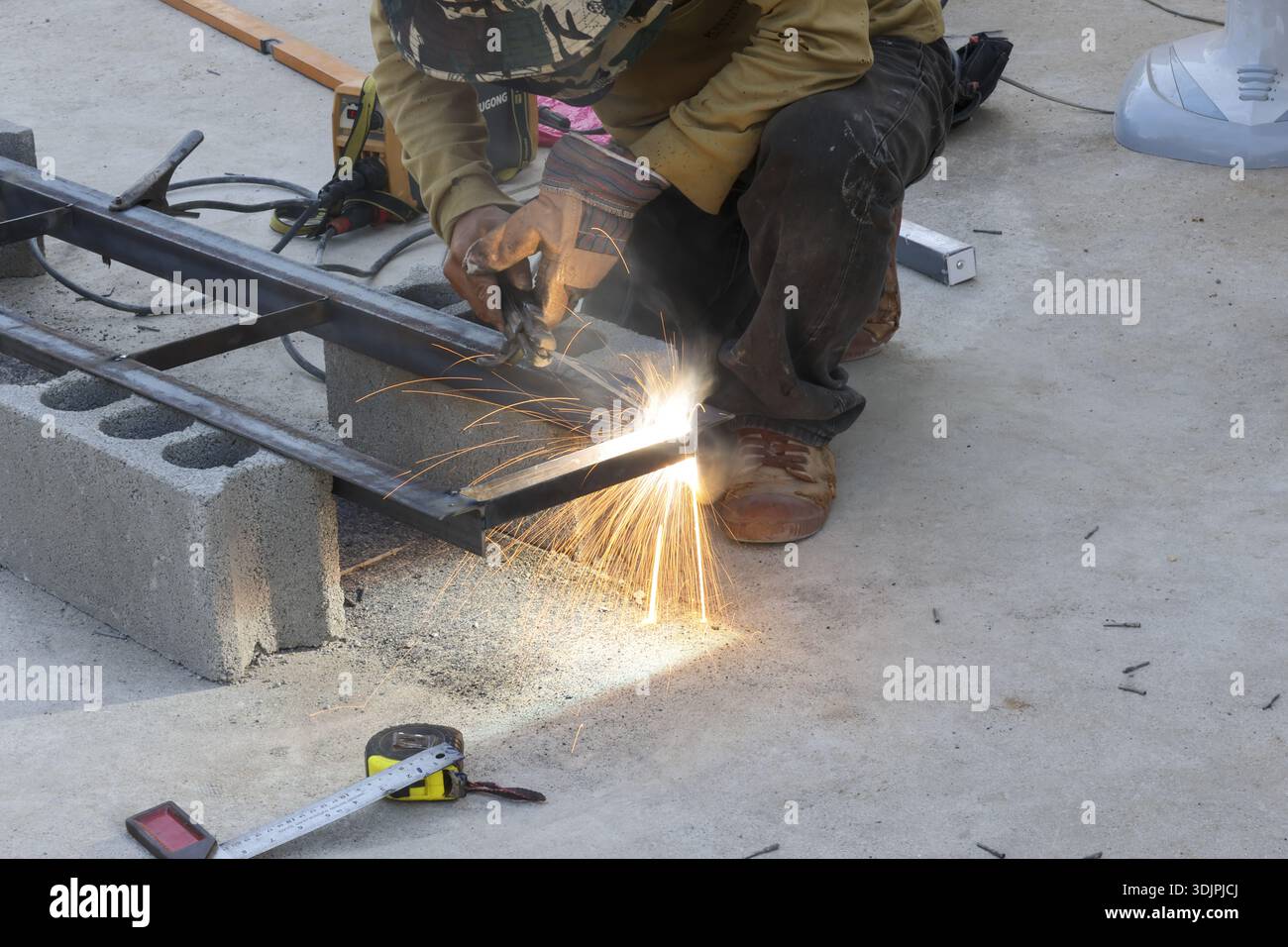 Focused male welder working on metal frame construction project creating bright sparks with professional tool Stock Photo