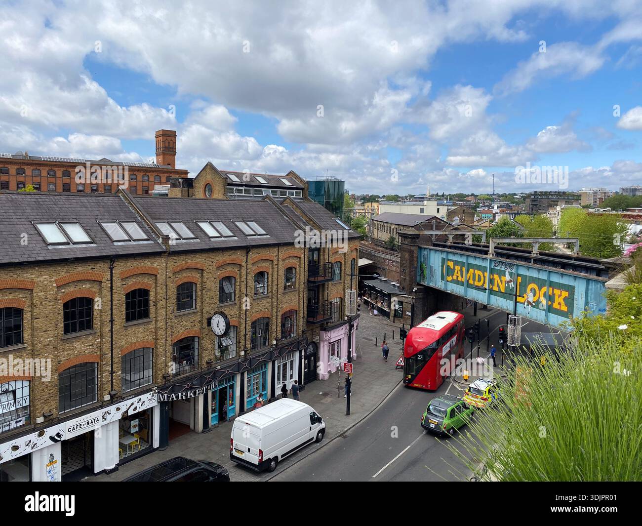 Elevated view of Camden Lock Market in London, featuring colourful graffiti bridge, brick warehouses, red double-decker bus, market stalls and pedestr - Smartphone Captured Stock Image