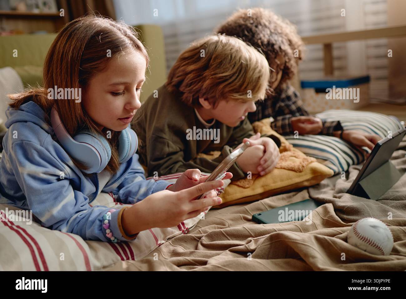 Generation Alpha Children Using Gadgets While Relaxing Indoors Together Stock Photo
