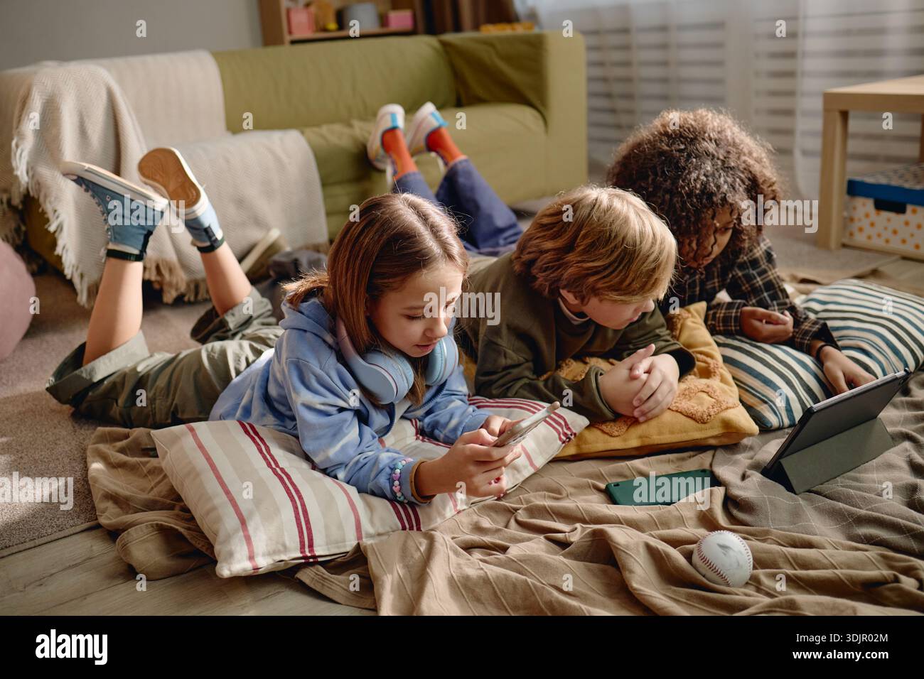Generation Alpha Children Using Gadgets While Lying on Floor Indoors Together Stock Photo
