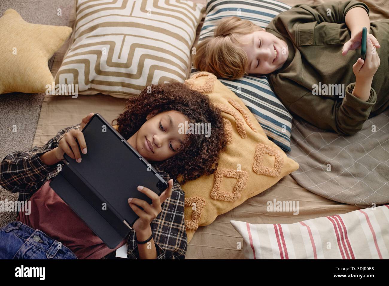 Multiethnic Generation Alpha Children Using Gadgets While Relaxing Indoors Stock Photo