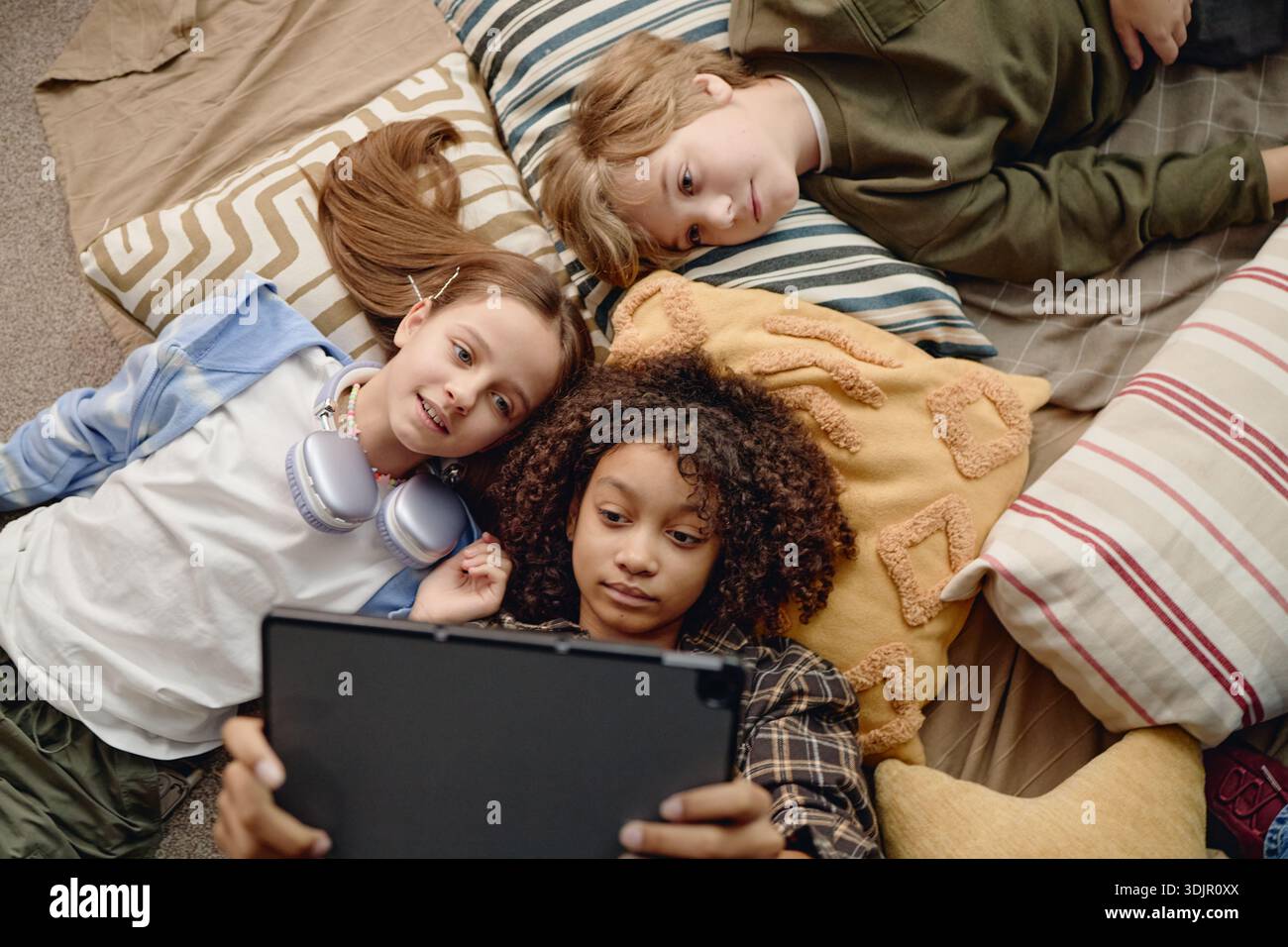 Multiethnic Generation Alpha Children Lying on Pillows Sharing Tablet Experience Stock Photo