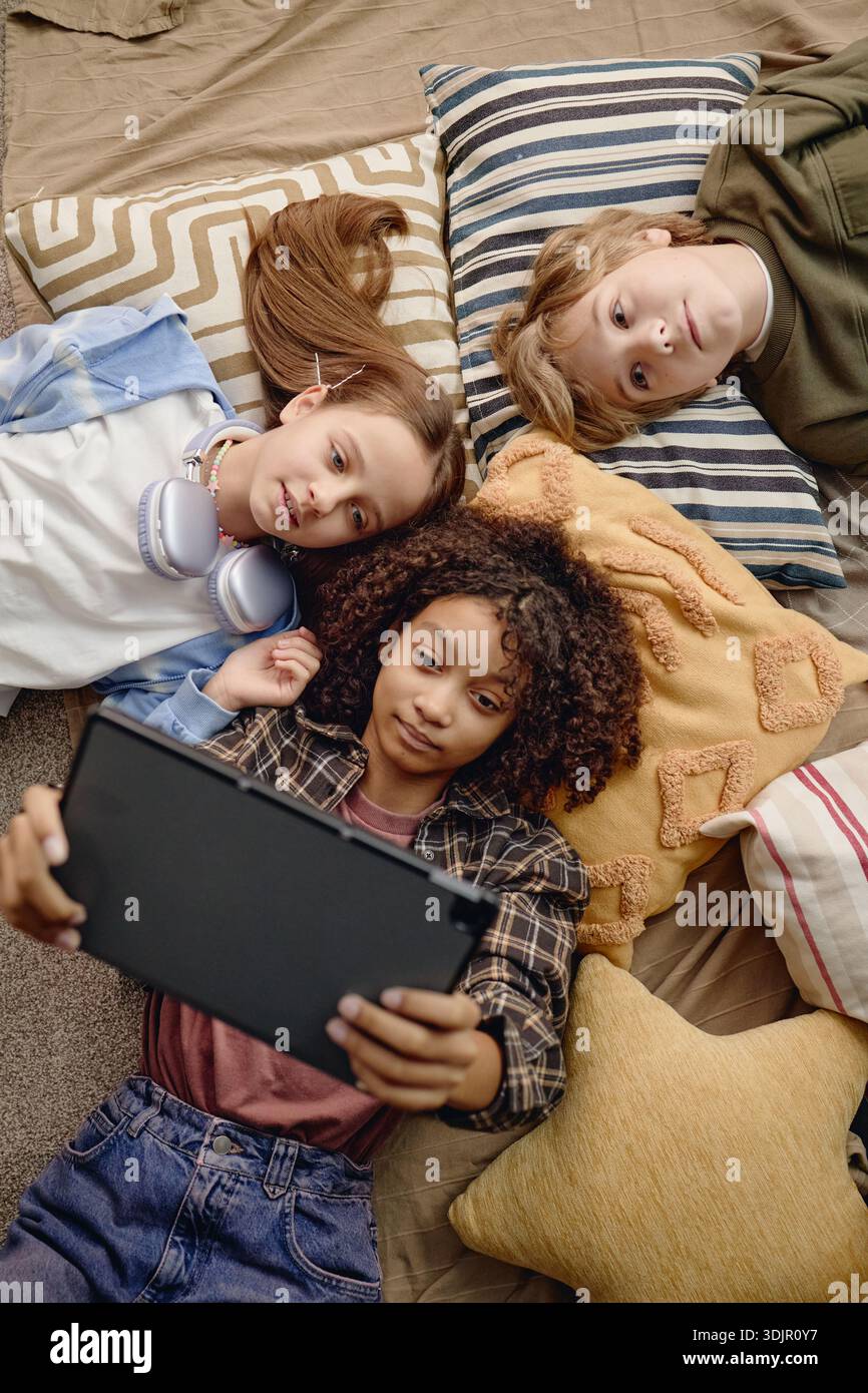 Multiethnic Generation Alpha Children Lying on Pillows Using Digital Tablet Stock Photo