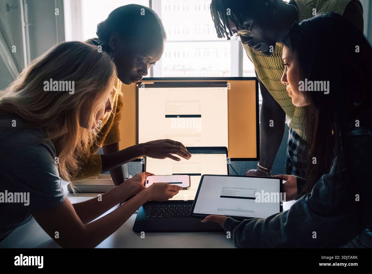 Female and male creative professionals comparing devices while working in tech office Stock Photo