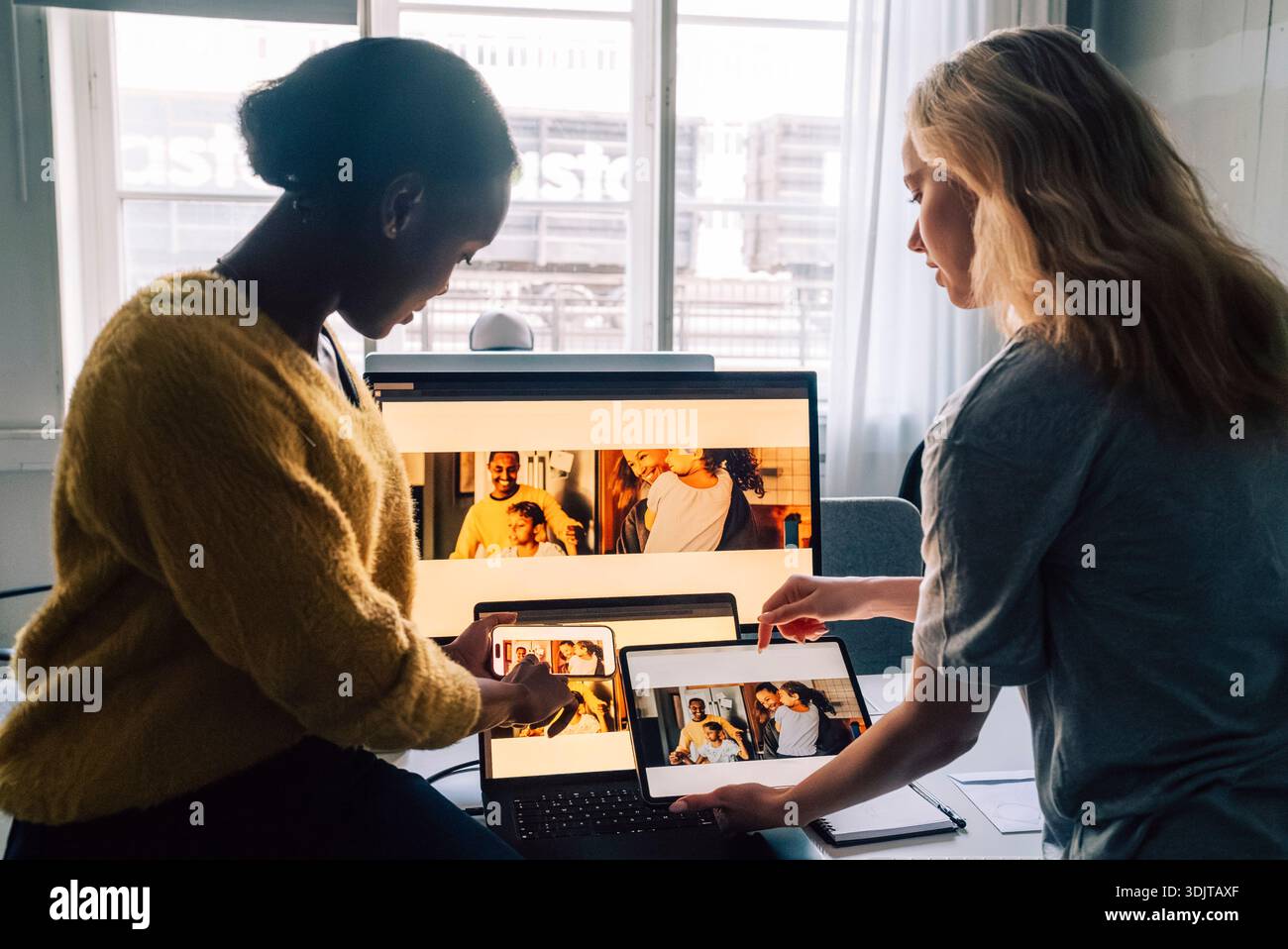 Female tech professionals checking software design preview by comparing them on different devices in office Stock Photo