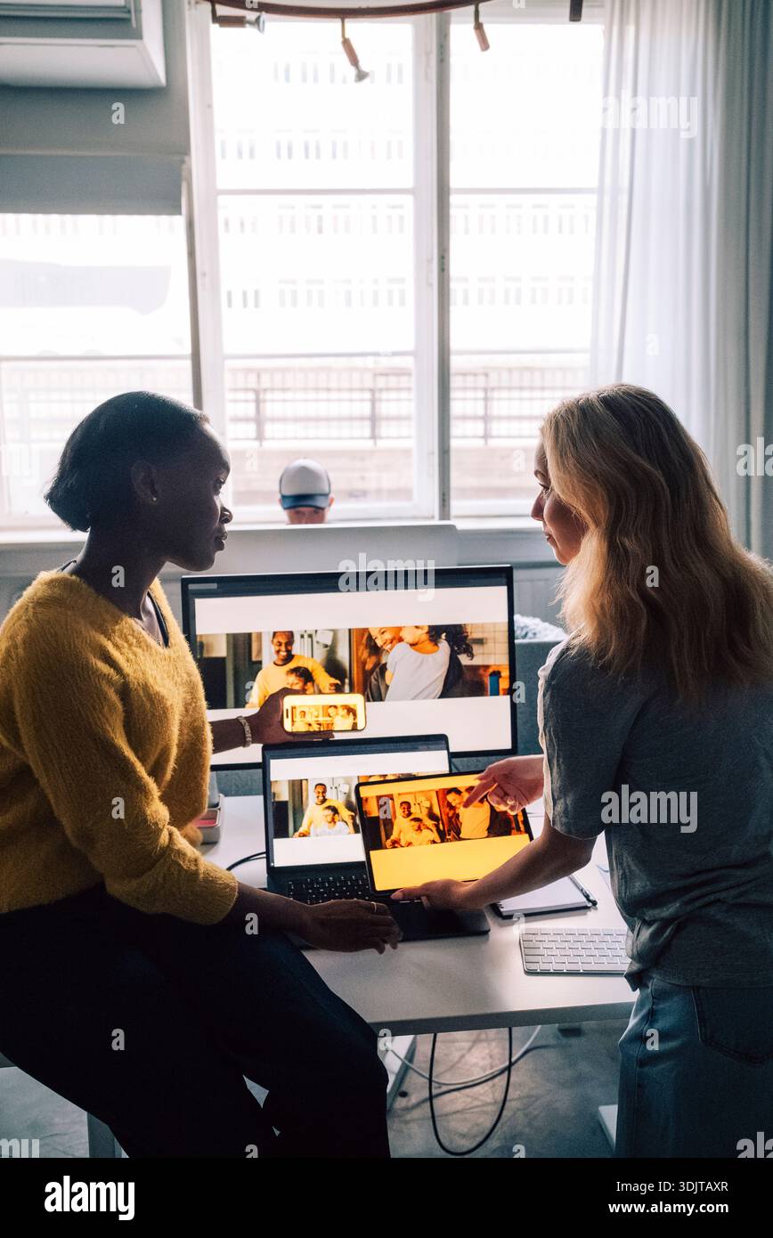 Female tech professionals discussing software design preview on different devices in office Stock Photo