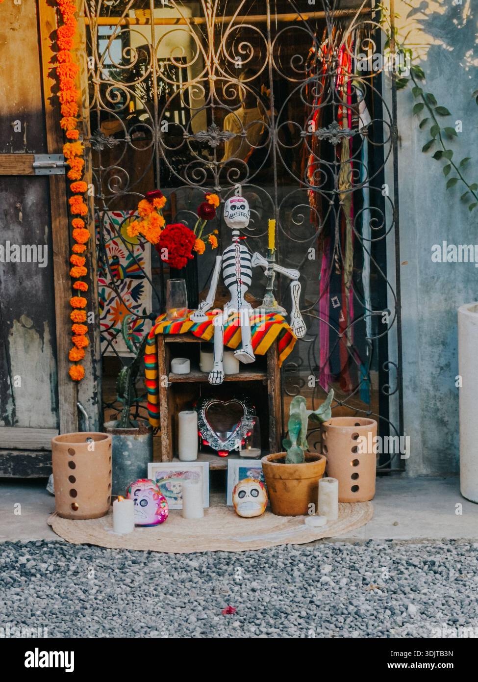 Traditional Day of the Dead–inspired altar displayed outdoors in Tulum, Mexico, featuring a seated skeleton figure, marigold flowers, candles, sugar s Stock Photo