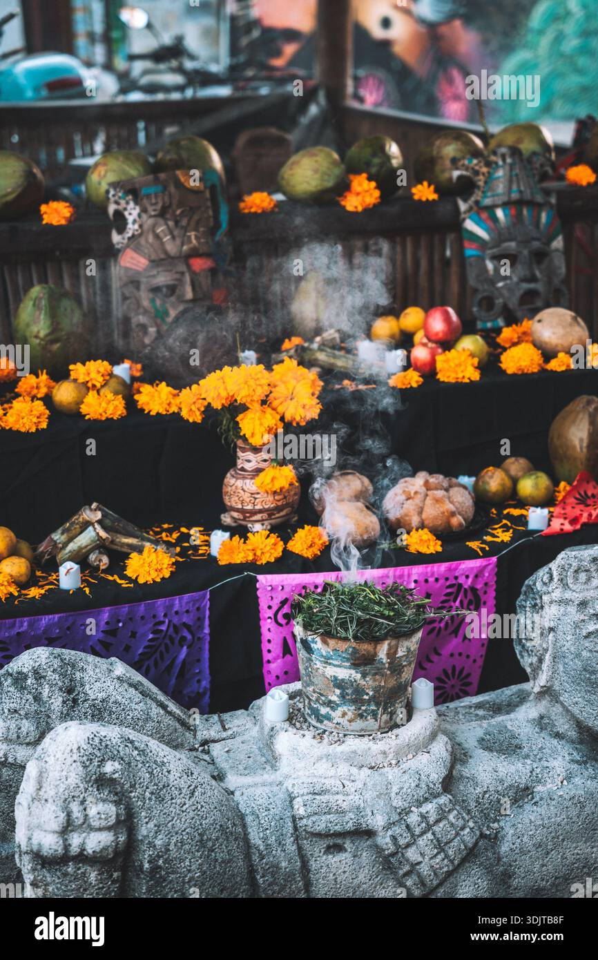 Dramatic Day of the Dead altar with burning incense, marigolds, ritual masks, fruit, and candles in Tulum, Mexico. Stock Photo