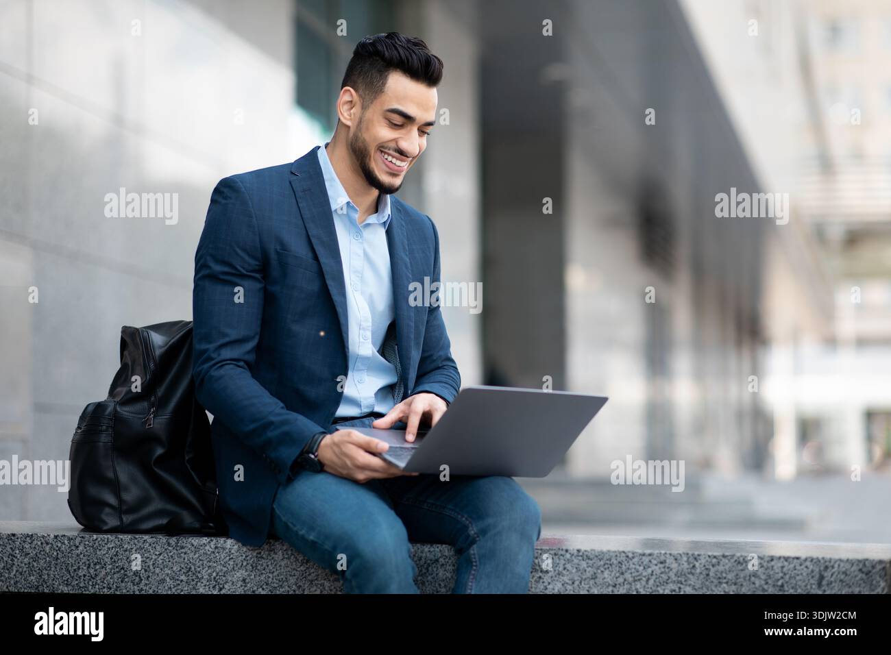 Positive middle eastern guy sitting on the street, using laptop Stock Photo