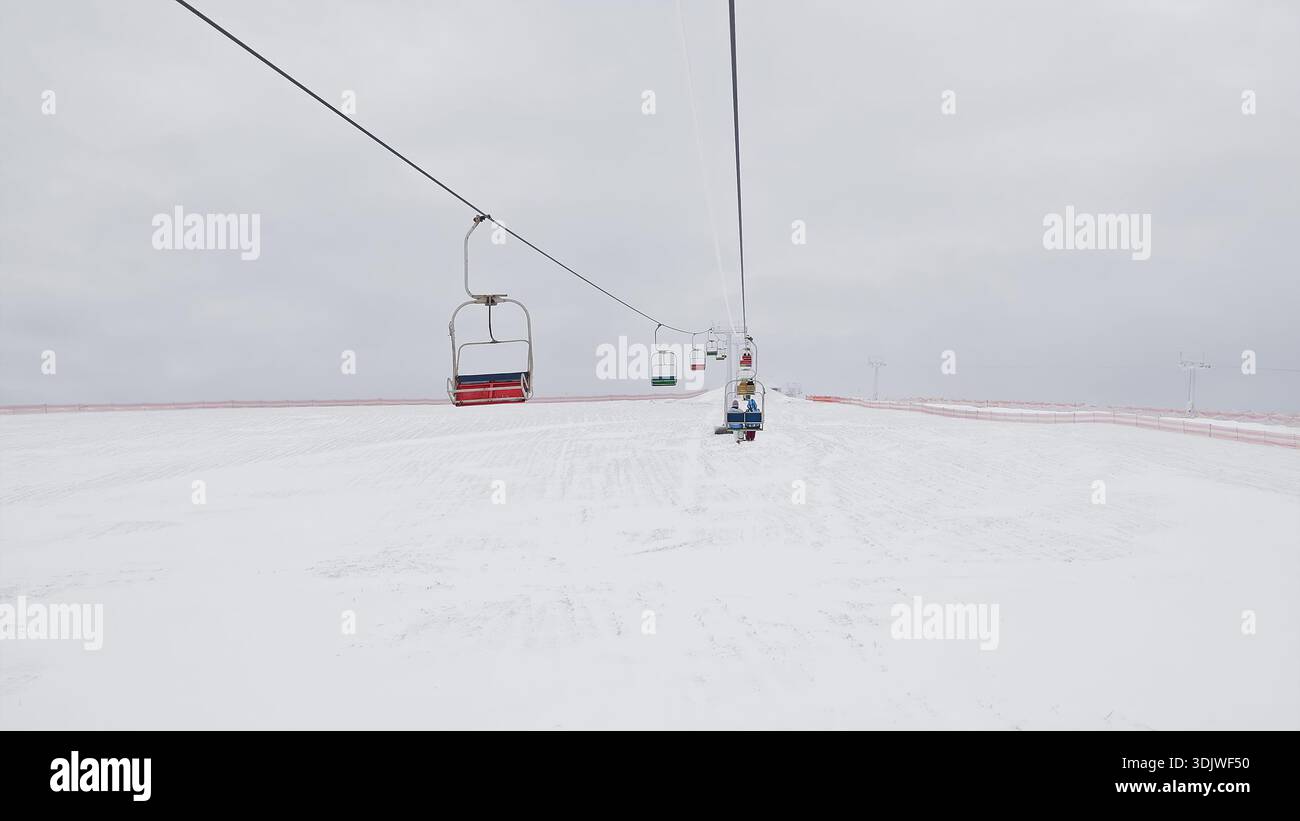 Ski lift with two skiers ascending snowy slope. Minimalist winter ...