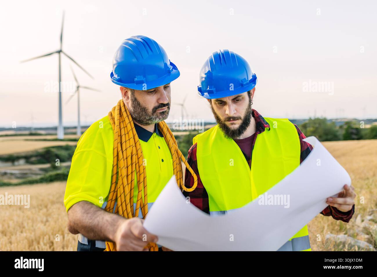 Engineers discussing wind turbine project blueprint on site Stock Photo